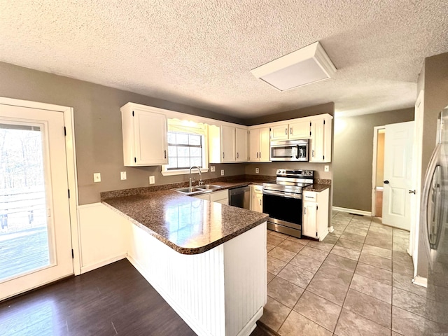 kitchen with stainless steel appliances, dark countertops, white cabinetry, a sink, and a peninsula