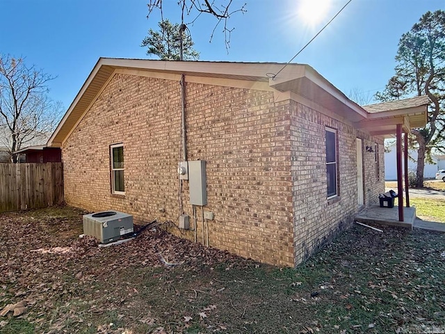 view of side of property with central AC, brick siding, and fence