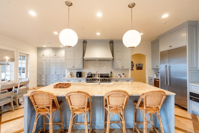 kitchen with arched walkways, stainless steel built in refrigerator, custom range hood, and gray cabinetry