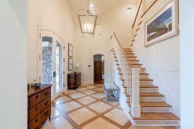 entryway featuring arched walkways, a notable chandelier, a towering ceiling, stairway, and baseboards