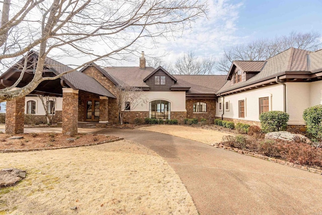 french country style house with concrete driveway, a chimney, stone siding, and stucco siding