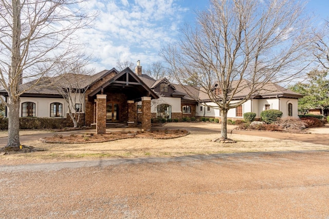 view of front of home with driveway, a chimney, stone siding, and stucco siding