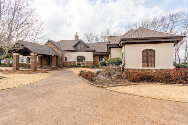 view of front of house featuring stone siding, a chimney, concrete driveway, and stucco siding