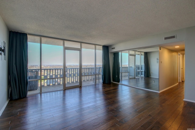 spare room with a wealth of natural light, visible vents, a wall of windows, and dark wood-type flooring