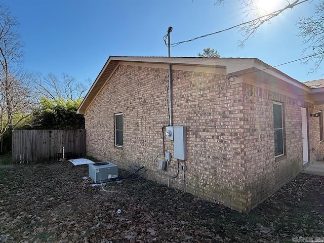 view of side of property featuring brick siding, cooling unit, and fence