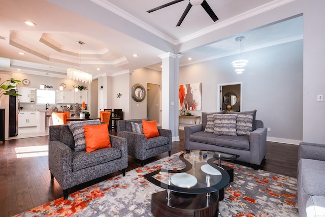 living area featuring ornamental molding, a tray ceiling, dark wood-style flooring, and ornate columns