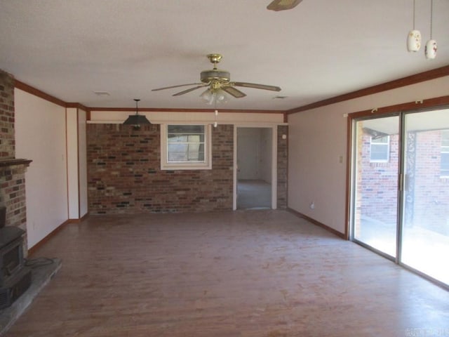 unfurnished living room with ornamental molding, a wood stove, brick wall, and a ceiling fan