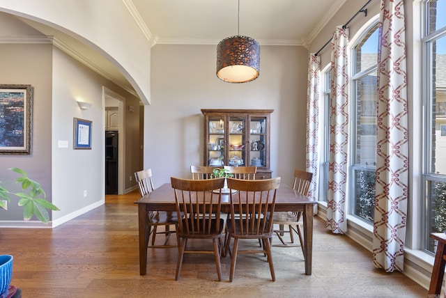 dining area with baseboards, arched walkways, crown molding, and wood finished floors