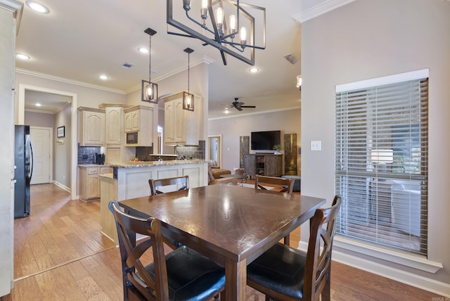 dining room featuring visible vents, a ceiling fan, ornamental molding, light wood-style floors, and a fireplace