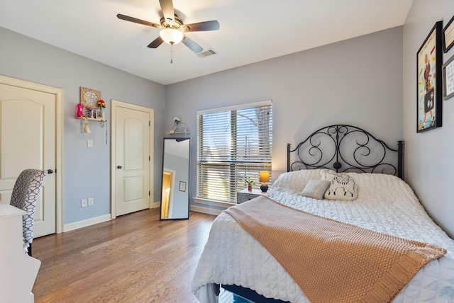 bedroom with a ceiling fan, baseboards, visible vents, and wood finished floors