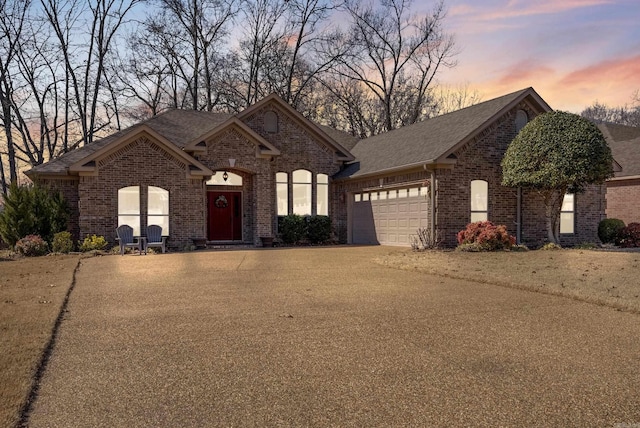 french country home with driveway, a garage, and brick siding