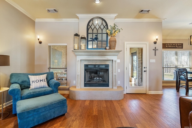 living area with a fireplace with raised hearth, ornamental molding, wood finished floors, and visible vents