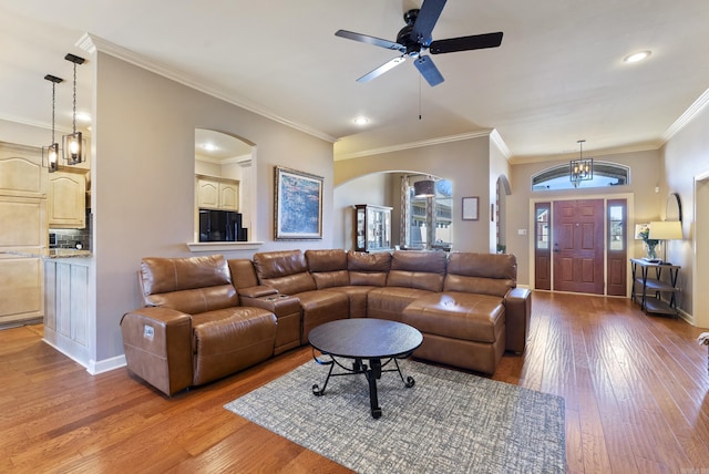 living room featuring light wood-style floors, arched walkways, ornamental molding, and baseboards