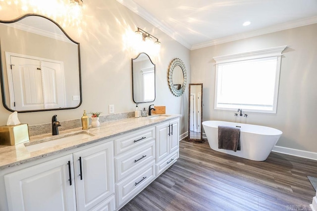 bathroom with ornamental molding, a sink, a freestanding bath, and wood finished floors