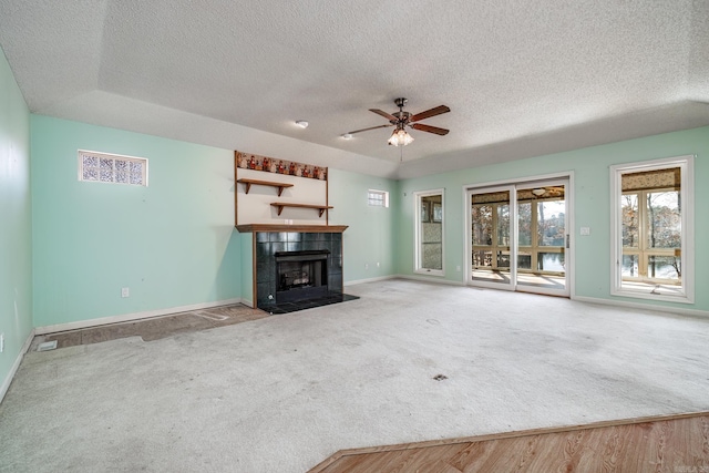 unfurnished living room featuring baseboards, a tile fireplace, ceiling fan, a textured ceiling, and carpet flooring