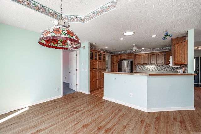 kitchen with light wood-style floors, freestanding refrigerator, a peninsula, and white microwave