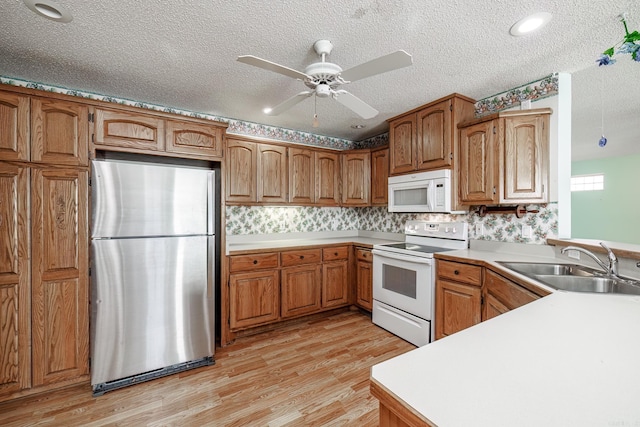 kitchen with white appliances, light wood-style flooring, brown cabinetry, and a sink