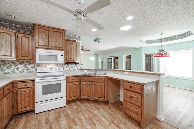 kitchen featuring a peninsula, white appliances, a sink, and light wood-style flooring