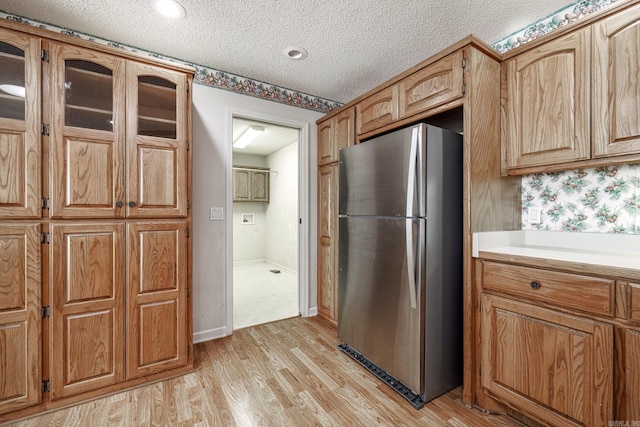 kitchen featuring light countertops, light wood-style floors, freestanding refrigerator, glass insert cabinets, and a textured ceiling