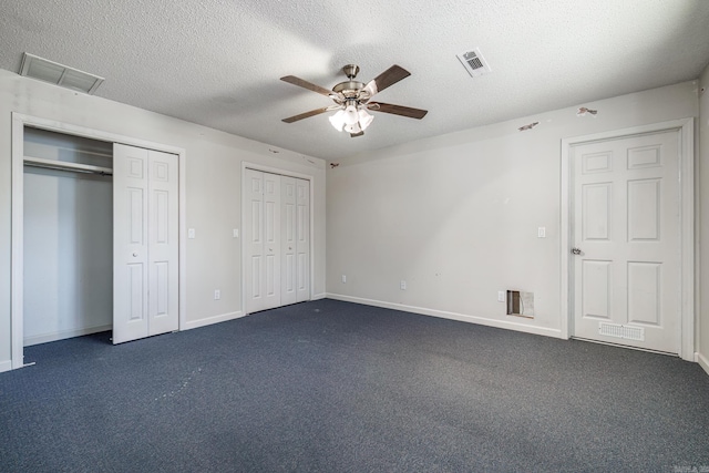 unfurnished bedroom with multiple closets, dark colored carpet, visible vents, and a textured ceiling