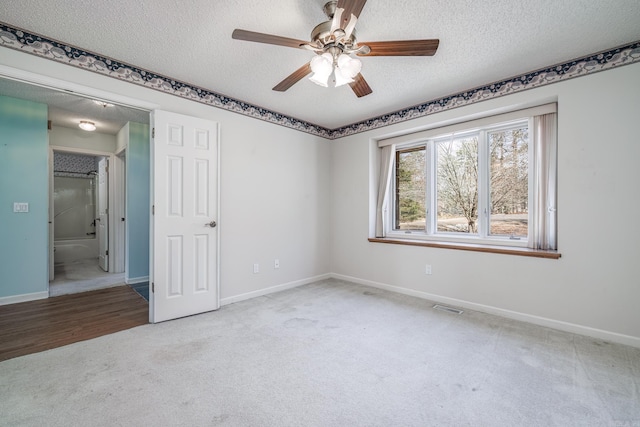 carpeted spare room with baseboards, visible vents, ceiling fan, and a textured ceiling