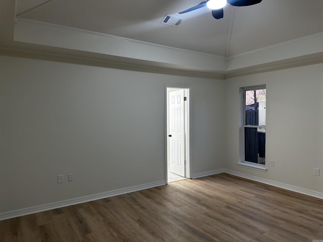 spare room featuring a raised ceiling, wood finished floors, visible vents, and baseboards