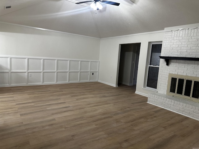 unfurnished living room featuring a ceiling fan, lofted ceiling, ornamental molding, wood finished floors, and a brick fireplace