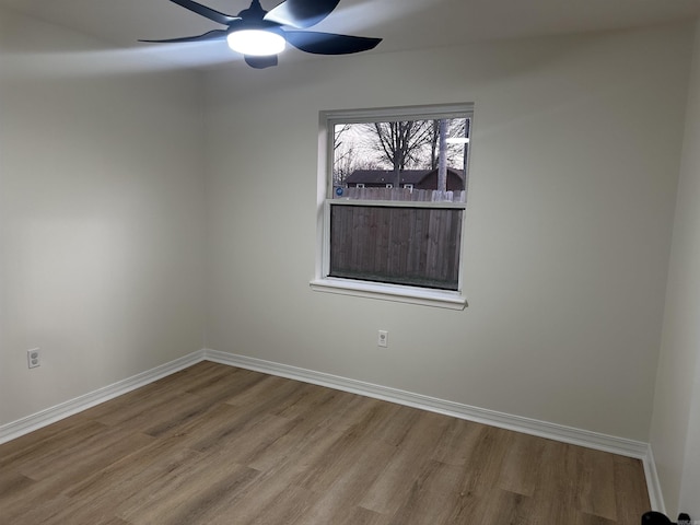 empty room with wood finished floors, a ceiling fan, and baseboards