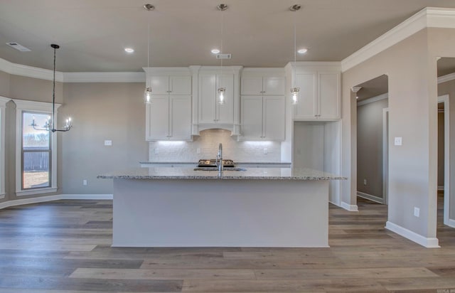 kitchen featuring wood finished floors, white cabinetry, ornamental molding, backsplash, and an island with sink