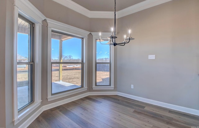 unfurnished dining area featuring a chandelier, dark wood-type flooring, ornamental molding, and baseboards