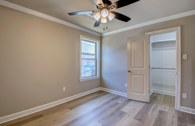 unfurnished bedroom featuring light wood finished floors, a spacious closet, ornamental molding, and baseboards