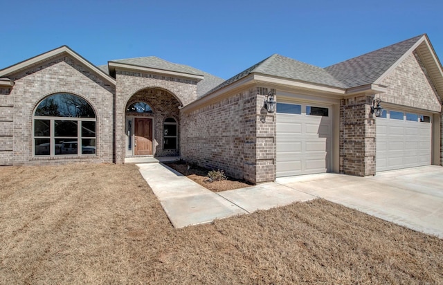 french country inspired facade with driveway, brick siding, an attached garage, and a shingled roof