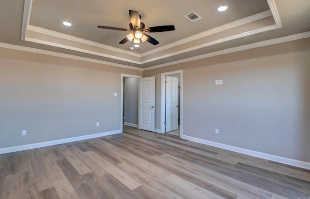 spare room featuring a raised ceiling, visible vents, light wood finished floors, and baseboards