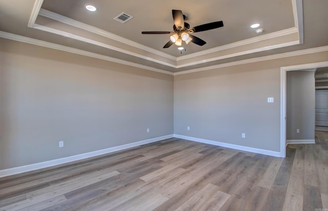 spare room with wood finished floors, a raised ceiling, visible vents, and baseboards