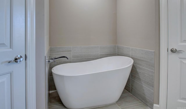 bathroom with tile walls, a freestanding bath, and wainscoting