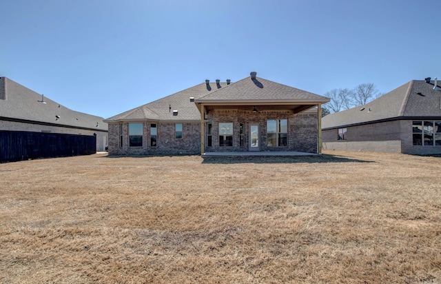 back of house featuring brick siding, a shingled roof, a patio, and a yard