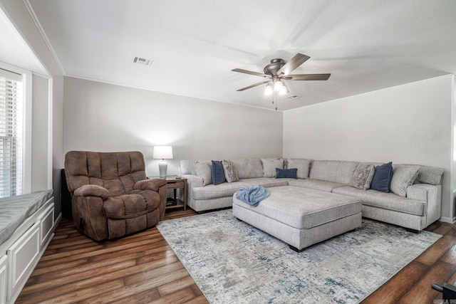 living area featuring ornamental molding, dark wood finished floors, visible vents, and a ceiling fan