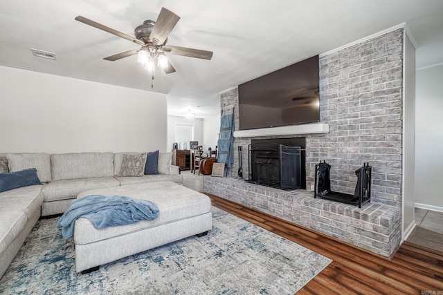 living area with visible vents, ceiling fan, ornamental molding, wood finished floors, and a fireplace