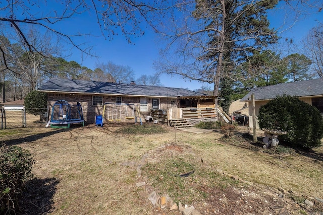 back of property with a deck, a trampoline, fence, and a gate