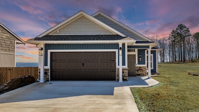 view of front of house featuring a shingled roof, concrete driveway, stone siding, an attached garage, and fence