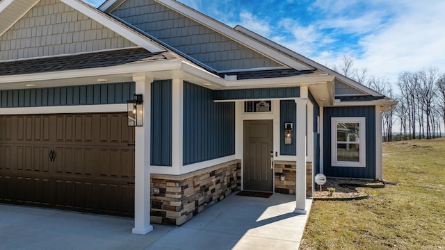 doorway to property featuring a garage, stone siding, a shingled roof, and concrete driveway