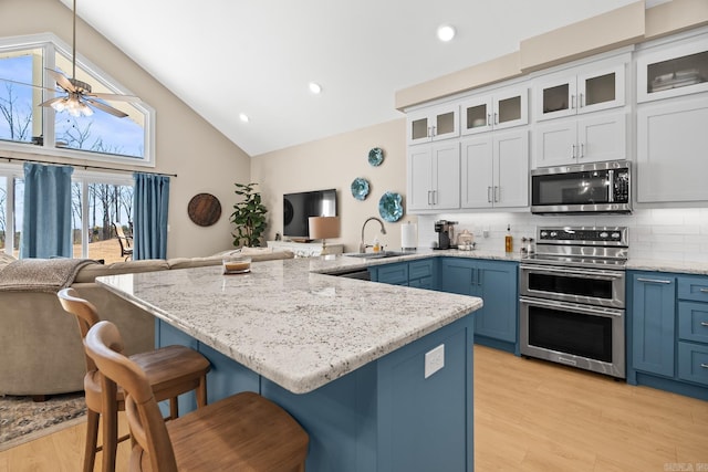 kitchen with a breakfast bar, appliances with stainless steel finishes, open floor plan, a sink, and blue cabinets