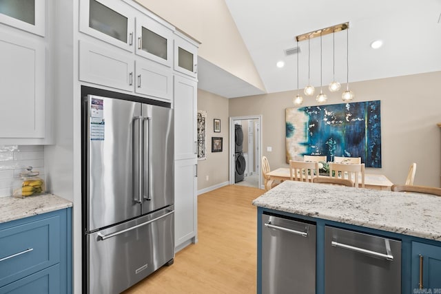 kitchen featuring high end refrigerator, visible vents, vaulted ceiling, tasteful backsplash, and stacked washer and clothes dryer