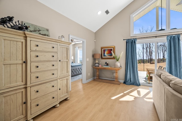 living area with light wood-style floors, visible vents, high vaulted ceiling, and baseboards