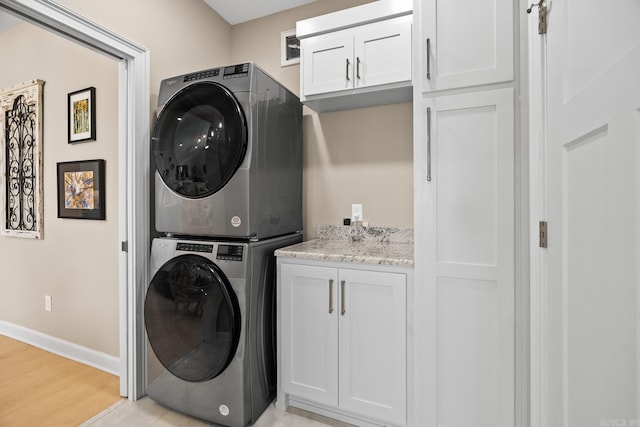 washroom featuring light wood finished floors, cabinet space, stacked washer and clothes dryer, and baseboards