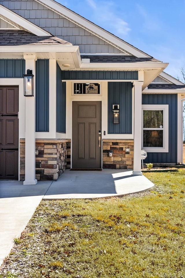 view of exterior entry featuring a lawn, stone siding, roof with shingles, a porch, and board and batten siding