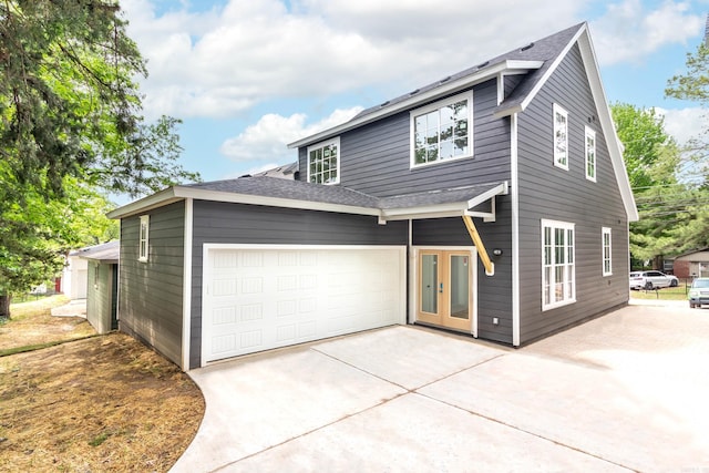 view of front facade featuring a garage, french doors, a shingled roof, and concrete driveway