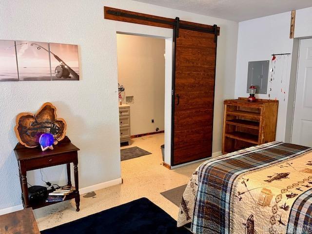 bedroom featuring electric panel, baseboards, and a barn door