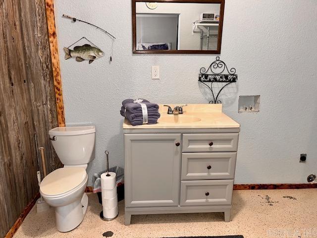 half bathroom featuring baseboards, a textured wall, toilet, speckled floor, and vanity