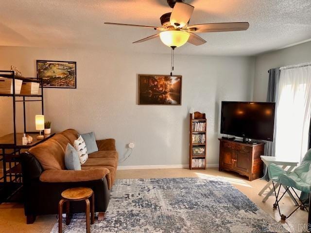 living area with ceiling fan, a textured ceiling, and baseboards